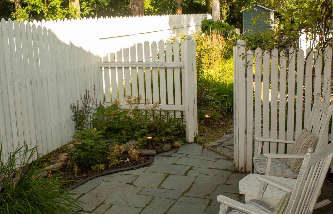 A flagstone path and white rocking chairs in the inn’s fenced garden
