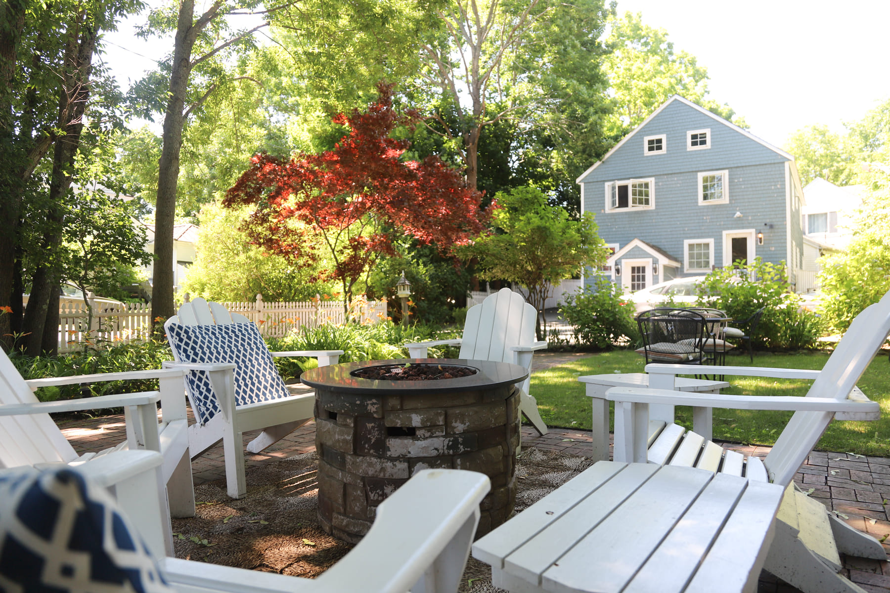 A circle of white Adirondack chairs around the stone fire pit