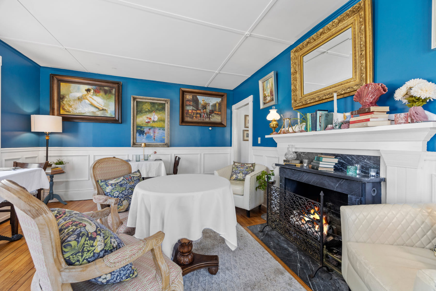 The blue front lounge with a lit marble fireplace and armchairs around a linen table