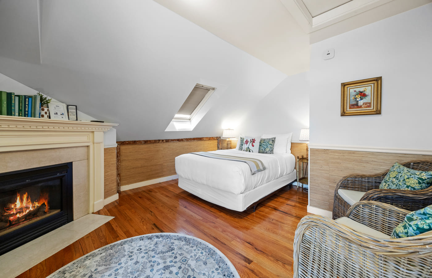 A skylit attic room with a lit fireplace and wicker seating