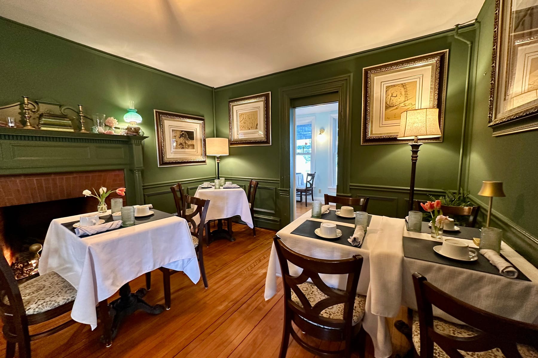 The green dining room with a lit fireplace and three linen-set tables